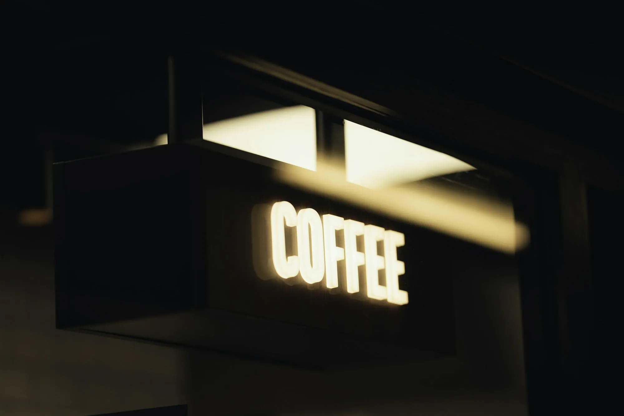 Illuminated projecting sign reading Coffee on a shopfront at night